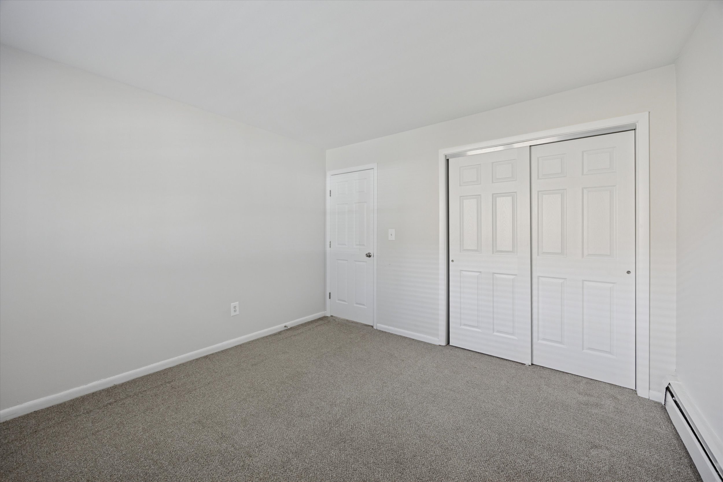 A room with white walls and a carpeted floor with two doors.